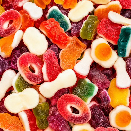 A close-up, top-down view of assorted gummy candies filling the frame, including red ring gummies, white bone gummies, orange bear gummies, green and purple gummy bears, and yellow and orange gummy eggs.